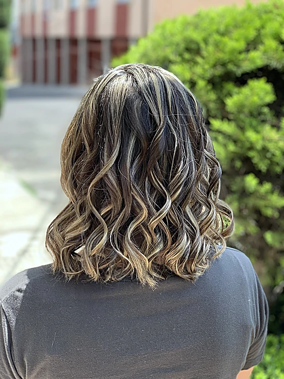 Corte a los hombros con rizos y luces, de espaldas, junto a un arbusto