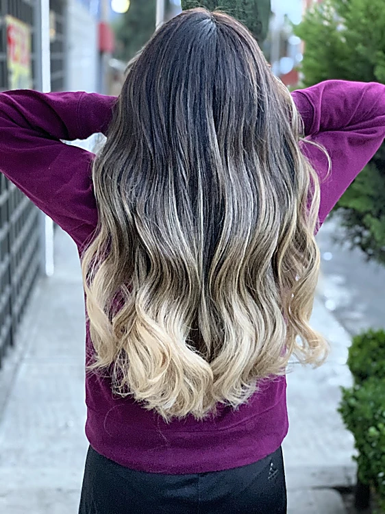 Cabello largo con degradado de raíz oscura a rubio platino, brazos arriba, en la calle