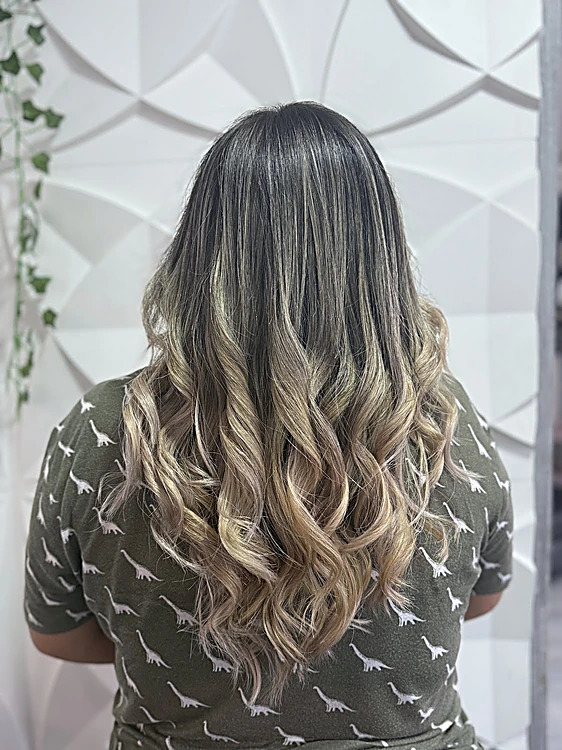 Ondas rubio ceniza con raíz oscura, de espaldas, frente al muro blanco con hiedra