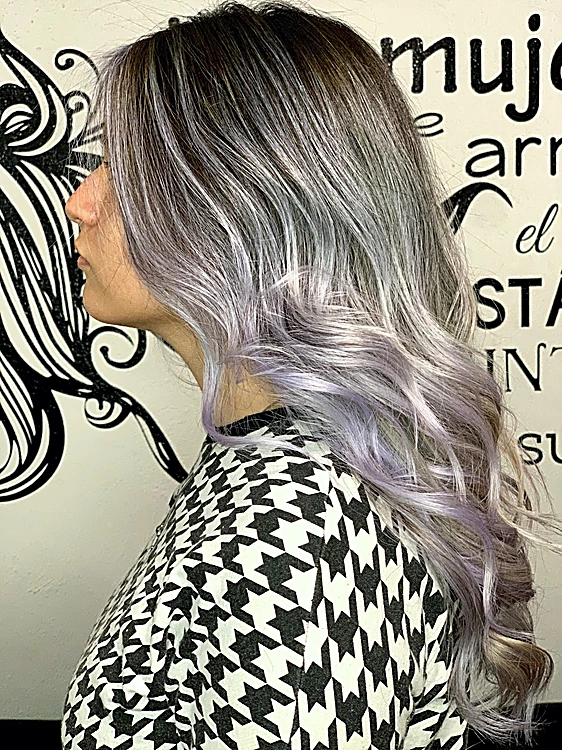 Clienta de perfil con cabello plata y lavanda sobre raíz oscura, frente a un mural negro de una mujer con melena en filigrana